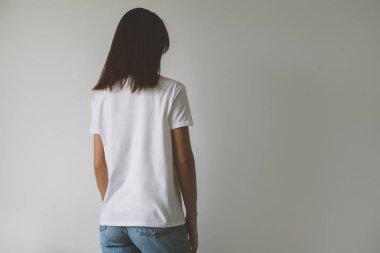 Arka planda, arkadan görünüm logo veya tasarım, beyaz tişört, beyaz duvar mock-up için boş alan ile beyaz t-shirt giyen genç hippi kız