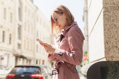 Başarılı kadın girişimci genç kadın cep telefonu dışında tarama cadde boyunca yürüyüş cep telefonu kablosuz bağlantı kullanarak, modern smartphone aygıtı kullanarak mutlu gülümseyen iş kadını