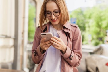 Başarılı kadın girişimci genç kadın cep telefonu dışında tarama cadde boyunca yürüyüş cep telefonu kablosuz bağlantı kullanarak, modern smartphone aygıtı kullanarak mutlu gülümseyen iş kadını