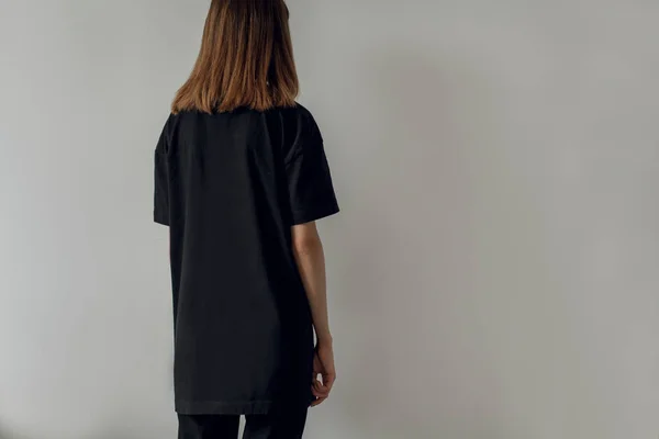 Genç hippi kız giyiyor siyah pantolon ve boş siyah t-shirt logo veya tasarım, model siyah t-shirt, arka plan, beyaz duvar için alan ile arkadan görünüm