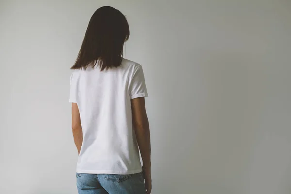 Arka planda, arkadan görünüm logo veya tasarım, beyaz tişört, beyaz duvar mock-up için boş alan ile beyaz t-shirt giyen genç hippi kız