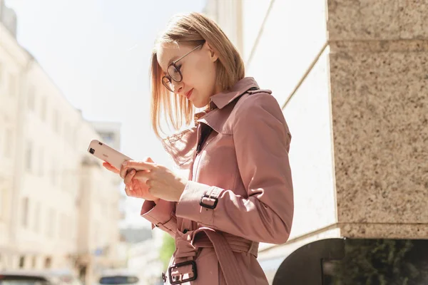 Başarılı kadın girişimci genç kadın cep telefonu dışında tarama cadde boyunca yürüyüş cep telefonu kablosuz bağlantı kullanarak, modern smartphone aygıtı kullanarak mutlu gülümseyen iş kadını