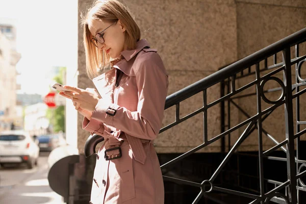 Başarılı kadın girişimci genç kadın cep telefonu dışında tarama cadde boyunca yürüyüş cep telefonu kablosuz bağlantı kullanarak, modern smartphone aygıtı kullanarak mutlu gülümseyen iş kadını
