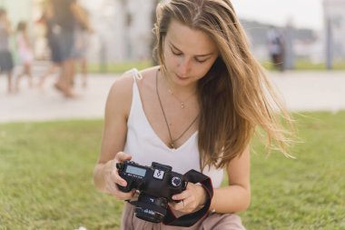 Genç ve güzel kız dslr kamera resim çekme ve ekran ayarları kontrol. Profesyonel kadın fotoğrafçı yolcu parkta fotoğraf makinesinde çekim. Yaz, yeşil park, açık havada