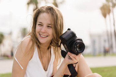 Pretty genç kız açık havada yaz güneşli günde parkta yürüyüş, seyahat, fotoğraf, yapım profesyonel dslr fotoğraf makinesi fotoğraf bir hobi olarak fotoğraf çekimi sırasında gülüyor kameraya bakıyor