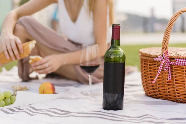 Boş bir şişe kırmızı şarap yakın çekim. Arka plan üzerinde piknik kız. Sana logo veya tasarım için alan. Açık havada yemek ve zevk tatiller ve hafta sonları Park yeşil çim ile olan kadın