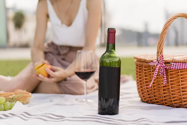 被裁剪的黑色红酒瓶的图像 美丽的女人在公园里野餐 坐在绿色的草地上 和朋友们在背景上庆祝节日 空间为您标志或设计 — 图库照片