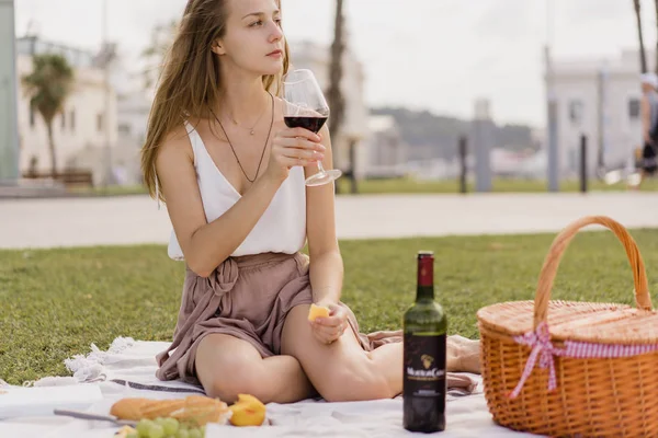 Tatil ve yaz zevk ve temiz havada rahatlatıcı kırmızı şarap içme ve yeme peynir ve aperatifler, yeşil çimenlerin üzerinde oturan parkta piknik güzel kadın