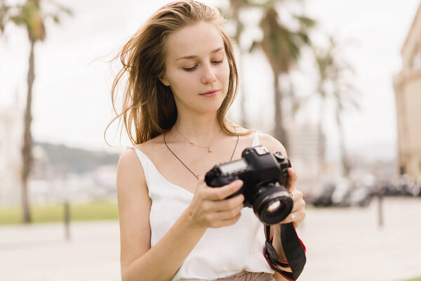 Professional female photographer taking pictures on a modern dslr camera in the park while walking around in the fresh air, young traveller girl using photo camera and shooting landscapes