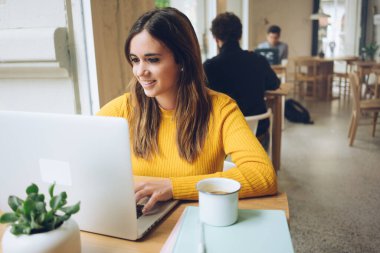 Kahveli ve defterli neşeli hipster blogcu dizüstü bilgisayarında bedava kablosuz internete bağlı Emale mesajı okuyor. Modern cihazlarla online yayın yapan pozitif genç öğrenci 