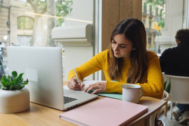 Genç kız öğrenci taşınabilir netbook 'tan bilgi yazarken üniversite kampüsündeki derslere hazırlanıyor. Hippi kız kafede otururken dizüstü bilgisayarda çalışıyor.