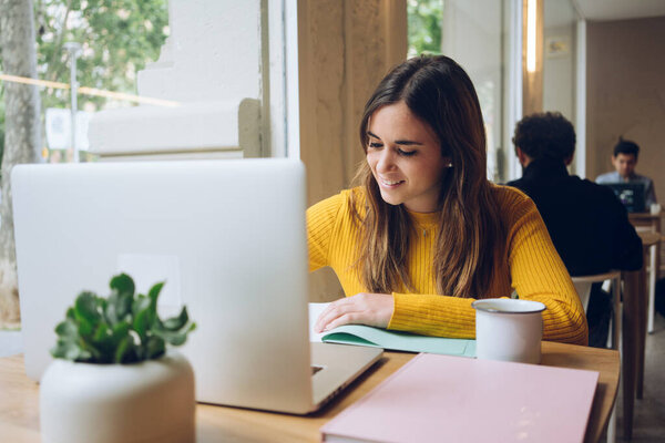 attractive business woman sitting at table in cafe and writing in notebook. Using laptop, smartphone and cup of coffee. Freelancer working in coffee shop. Student learning online.