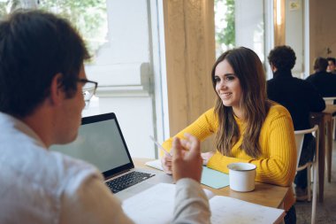 Takım çalışması. Güneşli bir günde kahvecide oturan iki genç serbest yazar yüksek hızlı 4G bağlantıya bağlı yeni web sitesi tasarımını model ekran ile tartışıyor.