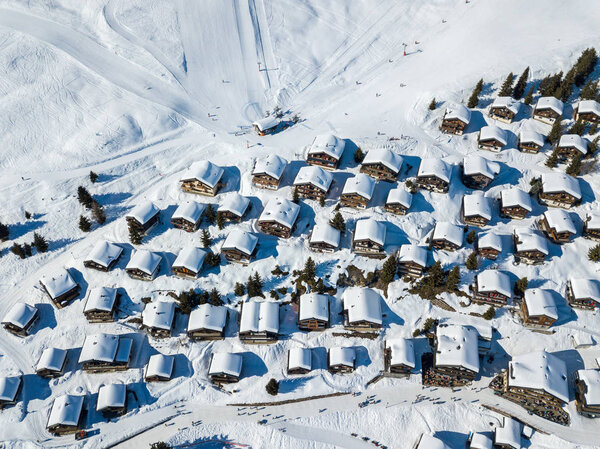 Aerial view of snow covered roofs over the traditional chalets with skiing lift station in the village of Swiss alps - taken by drone