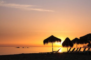 Palm şemsiye ve kanepeler, Girit Adası, Yunanistan ile plaj üzerinde güzel gün batımı