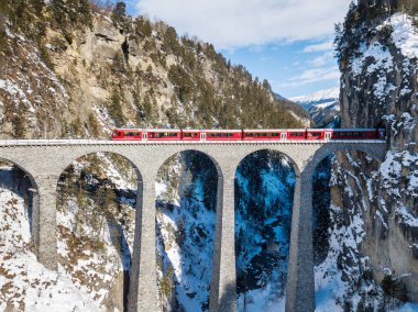 Filisur Switzerland - January 31. 2019: A red passenger Swiss train passing on the famous Landwasser Viaduct - an aerial image by drone