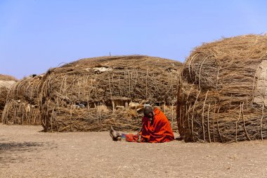 Serengeti, Tanzanya - 21 Eylül. 2012: Serengeti Milli Parkı'ndaki Massai köyündeki geleneksel kulübelerin önünde kırmızı kırmızı bir Massai kadını