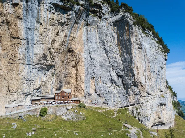 Aerial view of the guest house Aescher - Wildkirchli against the Ascher cliff at the mountain Ebenalp over the Swiss Alps in Appenzell region, Switzerland