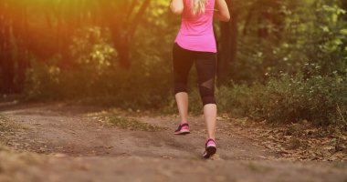 Genç fitness kadını sabah orman yolunda koşuyor. Motivasyon, yaşama uygun. Doğada güzel bir güneş ışığıyla koşan kişinin koşu ayakkabısı. Koşmadan önce kadın ısınıyor