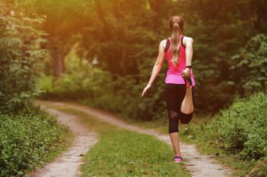 Genç fitness kadını sabah orman yolunda koşuyor. Motivasyon, yaşama uygun. Doğada güzel bir güneş ışığıyla koşan kişinin koşu ayakkabısı. Koşmadan önce kadın ısınıyor