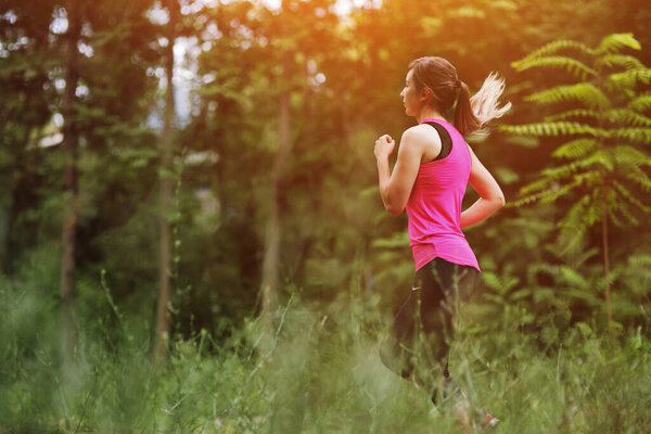 Young fitness woman running in the morning forest trail. Motivation healthy fit living. Running shoe of the person running in nature with beautiful sunlight. Woman warming up before running