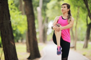 Genç kadın, doğa ormanında sporla meşgul. Sağlıklı bir yaşam sürüyor. Motivasyon, yaşama uygun. Koşu ayakkabısı. Güzel güneş ışığı. Koşmadan önce kadın ısınıyor