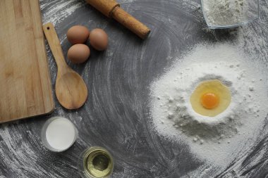 Kırık tavuk yumurtası un, zeytin yağı, süt, mutfak aleti gri masa arkasında. Fırın ürünleri için ürünler. Kesme tahtası, merdane, un eleği, tahta kaşık. ekmek ya da pasta