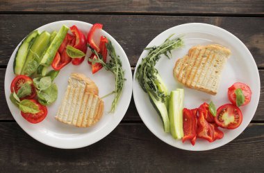 Sağlıklı organik sebze kahvaltısı, domates, tost, salata, fesleğen, salatalık, roka. Siyah ahşap bir masada beyaz tabakta vejetaryen sağlıklı yiyecekler. Yüksek kalite fotoğraf