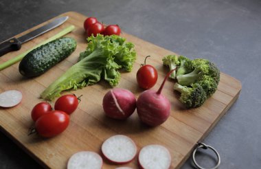 Gri bir masanın üzerinde taze sebzeler domates, marul, brokoli, turp.