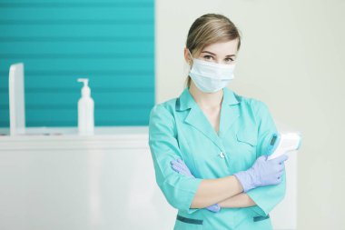 Hastanedeki koruyucu maskeli kadın doktor ya da hemşire pirometreyi elinde tutuyor. Koronavirüse karşı güvenlik önlemleri. Covid-19 önleme sağlık hizmeti konsepti. Steteskop boyunda..