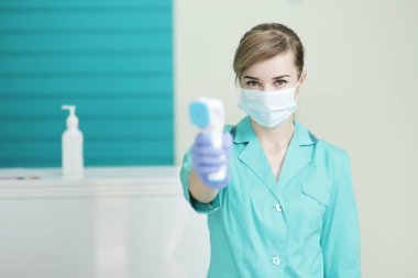 Hastanedeki koruyucu maskeli kadın doktor ya da hemşire pirometreyi elinde tutuyor. Koronavirüse karşı güvenlik önlemleri. Covid-19 önleme sağlık hizmeti konsepti. Steteskop boyunda..