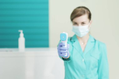 Hastanedeki koruyucu maskeli kadın doktor ya da hemşire pirometreyi elinde tutuyor. Koronavirüse karşı güvenlik önlemleri. Covid-19 önleme sağlık hizmeti konsepti. Steteskop boyunda..