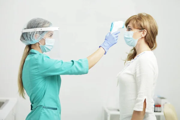 Mulher médica em medidas uniformes a temperatura de uma mulher com um pirômetro Imagem De Stock