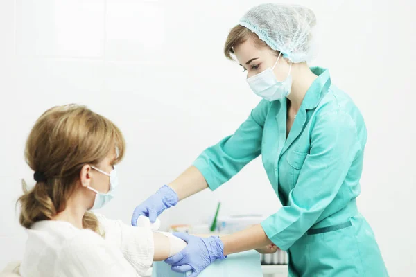 Eine Krankenschwester mit medizinischer Maske bindet einer Patientin die Hand — Stockfoto