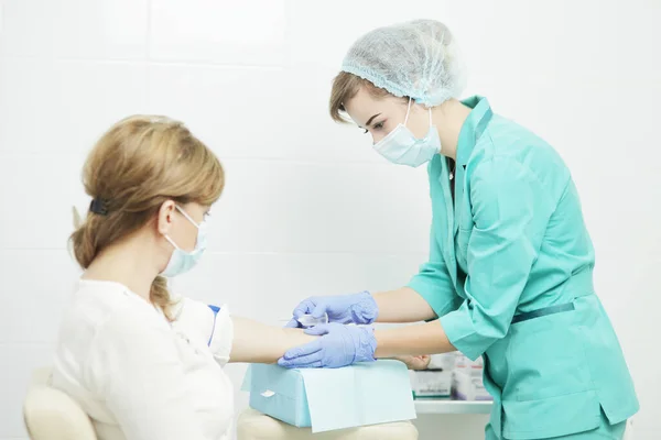 Eine Krankenschwester in medizinischer Maske entnimmt einer Patientin eine Blutprobe. lizenzfreie Stockfotos