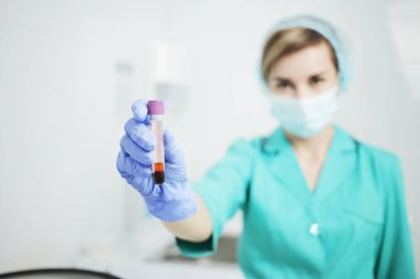 Tıbbi maskeli kadın hemşire kan testi için tüp tutuyor.