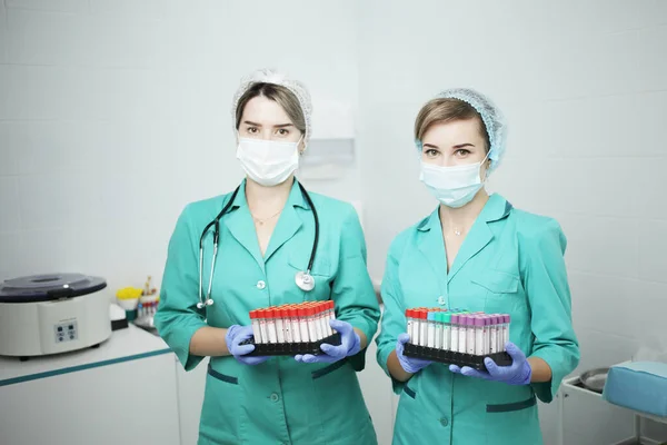 Deux infirmières médecins dans un masque médical tiennent des éprouvettes pour un test sanguin Image En Vente