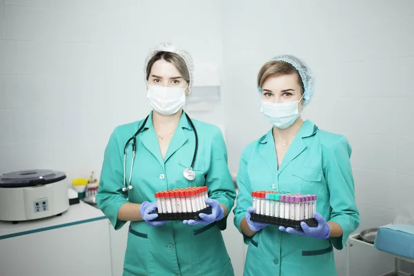 Twee vrouwelijke verpleegkundige arts in een medisch masker houden reageerbuisjes voor een bloedtest Stockfoto