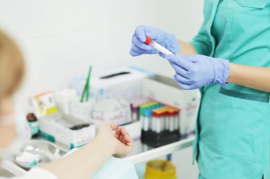 Tıbbi maskeli kadın hemşire kan testi için tüp tutuyor.