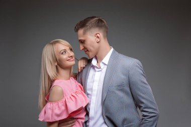Güzel çift birbirine bakarak ve düz gri arka plan üzerinde dururken gülümseyen.