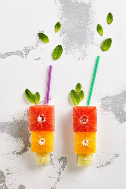 Taze narenciye - küp dilim portakal, Grapeftuit ve kireç. Bardağı taşıran damla içkiyle şekli. Yaratıcı yaz meyve düzeni. Üstten görünüm