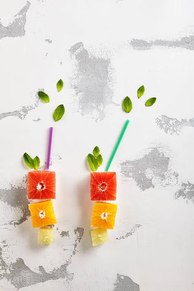 Taze narenciye - küp dilim portakal, Grapeftuit ve kireç. Bardağı taşıran damla içkiyle şekli. Yaratıcı yaz meyve düzeni. Üstten görünüm