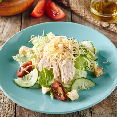 Sezar salatası tavuk, kruton, domates, salatalık mavi plaka üzerinde. Limon suyu, zeytinyağı ve ahşap rustik masa üzerinde Parmesan peyniri ile giyinmiş marul, yeşil salata