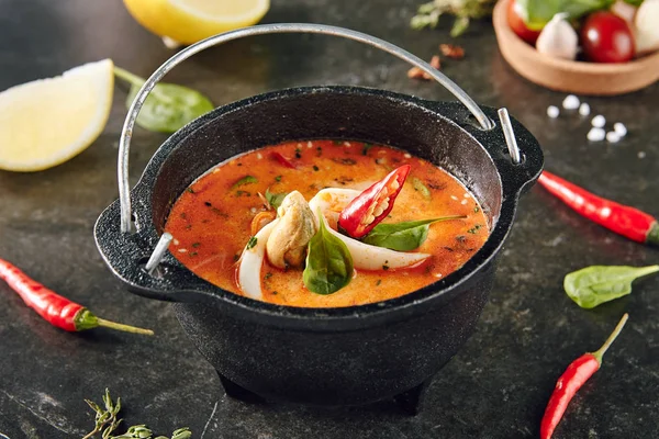 Tom Yum or Tom Yam with Squid, Shrimp, Chili Peppers, Lime Juice, Galangal, Fish Sauce, Lemongrass. Hot and Sour Thai Soup Cooked with Fragrant Spices. Traditional Thailand Food on Dark Background