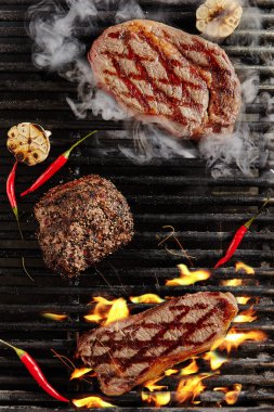 Hot Juicy Chivas Beef Steak on Barbecue Flames Grill Background. Smoked Ribeye Beef Steaks with Grilled Garlic, Spices and Red Peppers. Bbq Entrecote Meat Top View clipart