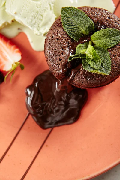 Hot Chocolate Fondant with Mint Leaves and Berries on Terracotta Plate Close Up. Fresh Brownie Dessert with Melted Dark Cocoa Mousse. Small Chocolate Cake with Crunchy Rind and Mellow Filling