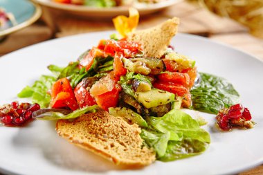 Barbekü ızgara patlıcan ya da patlıcan, kızarmış tatlı biber, nar taneleri, kruton, taze marul sebze salatası bırakır. Vegan Barbekü Mix beyaz yuvarlak plaka üzerinde Kapat