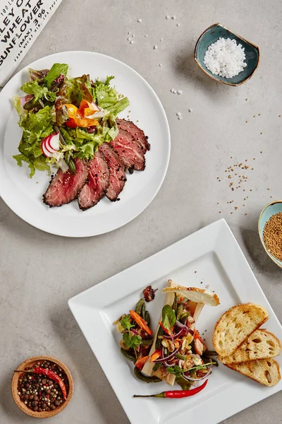 Izgara biftek salata veya yeşil karışımı ile Pazar rostosu. Kavrulmuş baharatlı kemik iliği tost ve sebze üstten görünüm ile kapatın. Sıcak Barbekü Orta nadir mermer et beyaz plaka üzerinde ince dilimler