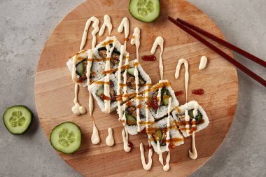 Uramaki suşi rulo beyaz baharatlı peynir sos kahverengi soya sosu en iyi manzaralı ve zirveye yerleşti. Nori Maki sette ince dilim salatalık ve yemek çubukları ile doğal ahşap arka plan