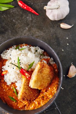 Köri ve pilav koyu arka plan en iyi görünümü ile sıcak baharatlı çıtır çıtır kızarmış tavuk fileto. Katsu veya Tonkatsu kırmızı Peppres, Türkiye'de et pirzola, ekmek kırıntıları, domates, biber sosu, susam, yeşillik ve otlar ile